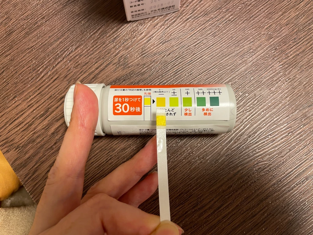 検査中の尿糖スティック。ケース側面のカラーチャートと色比較